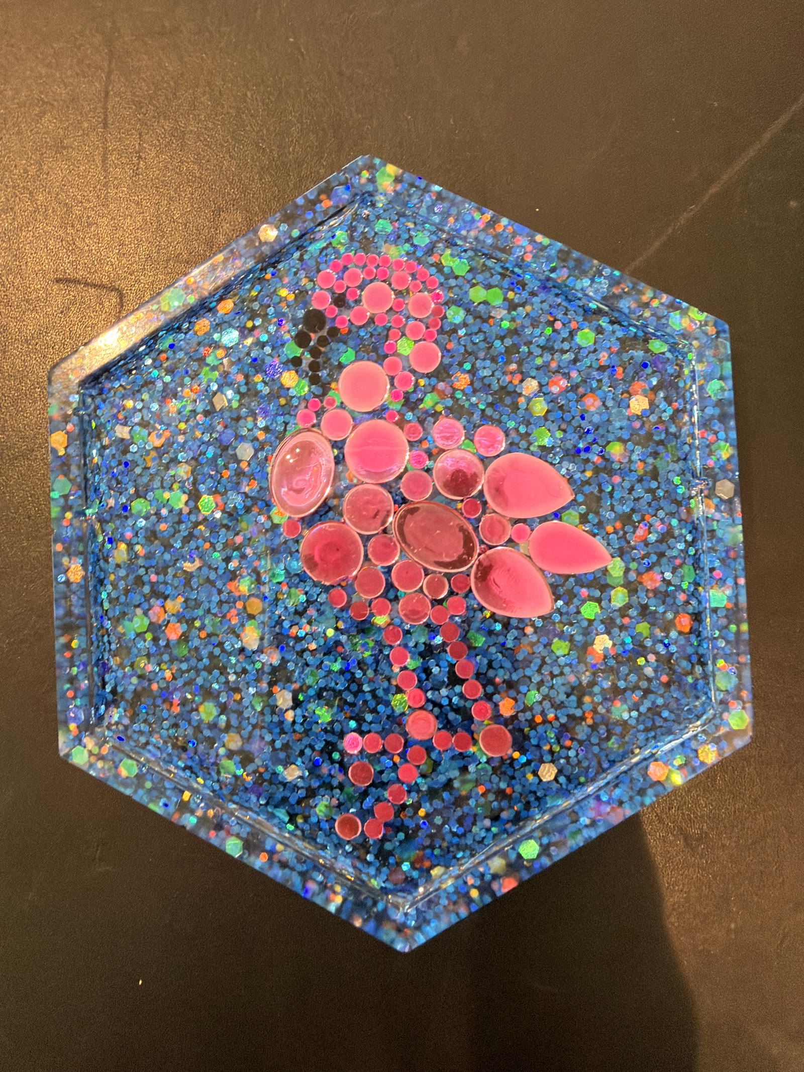 Hexagonal resin coaster with blue glitter and a pink flamingo mosaic made of gems
